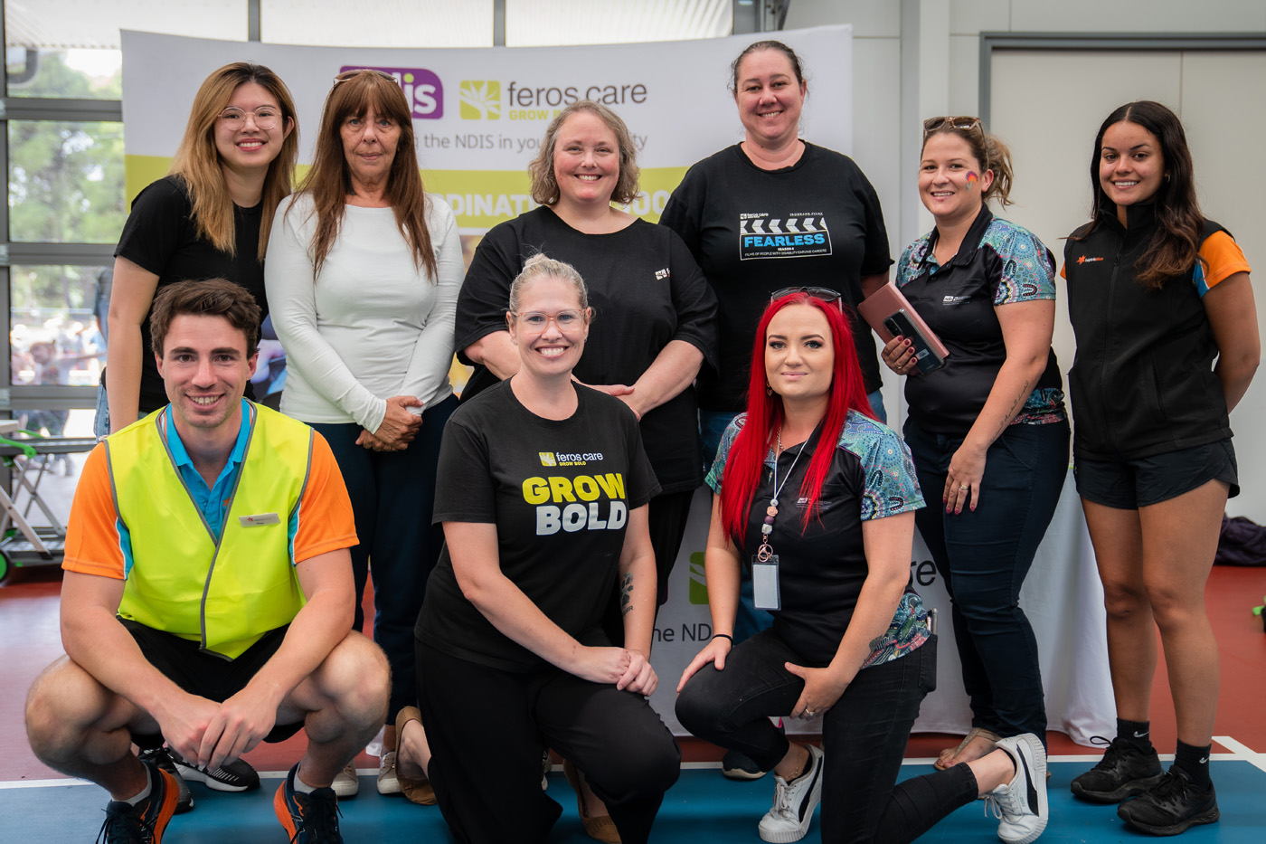 Nine people from Feros Care smiling to camera in front of Feros Care and NDIS banner.