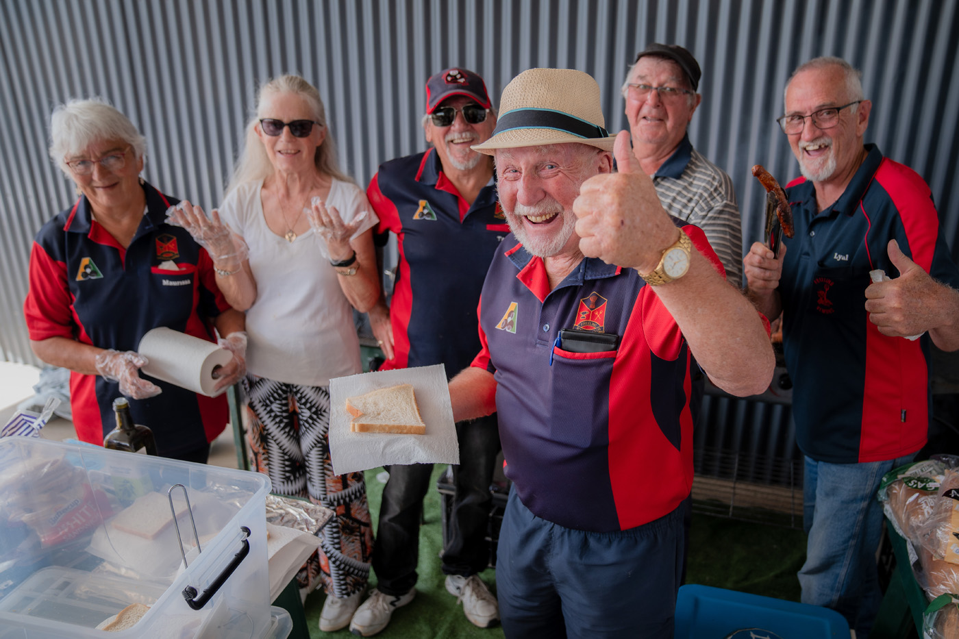 Six people standing around BBQ smiling at camera cooking sausage sizzle. Four people from Freeling Bowls Club.
